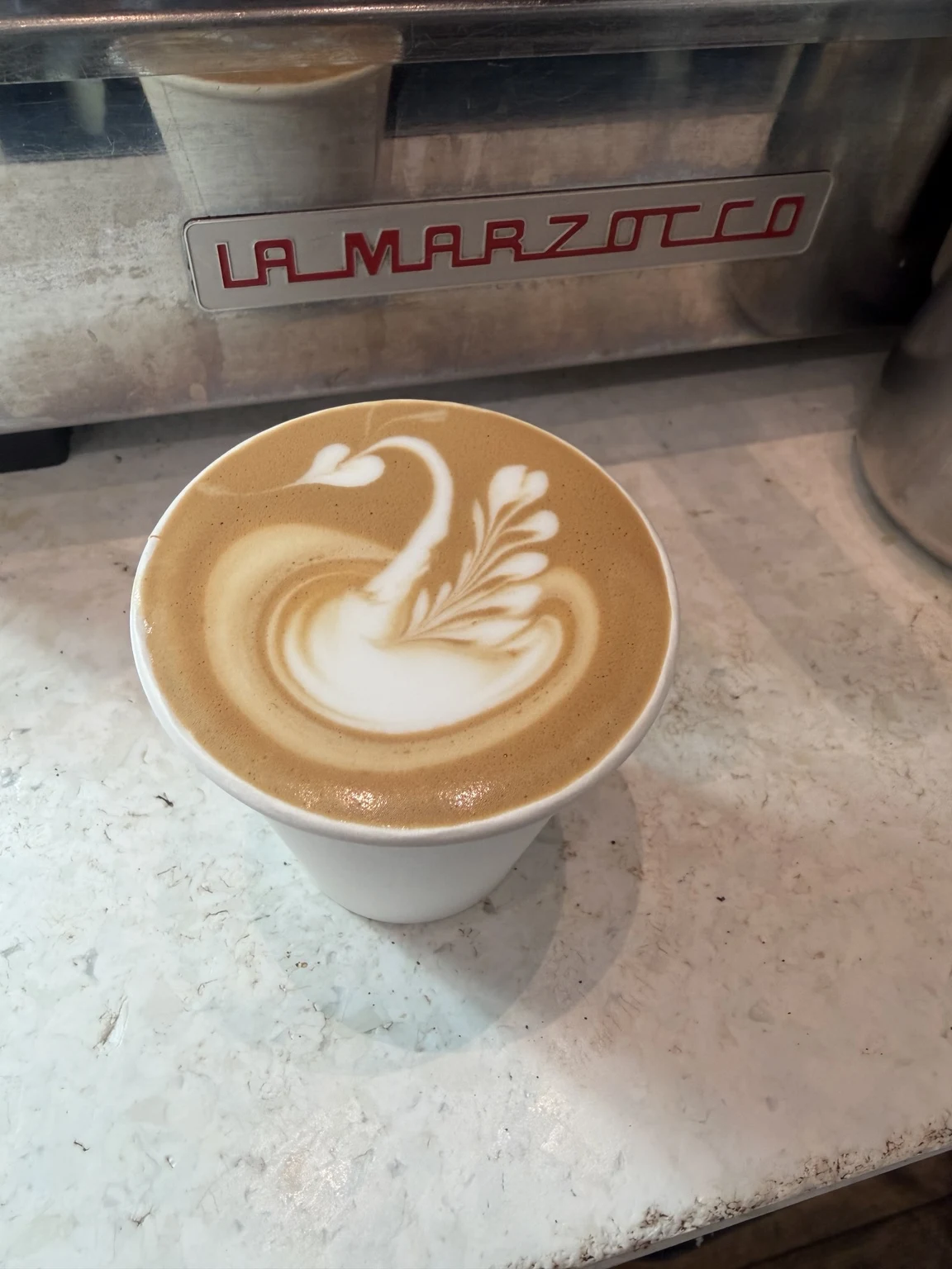 Swan latte art in a white cup in front of a La Marzocco machine