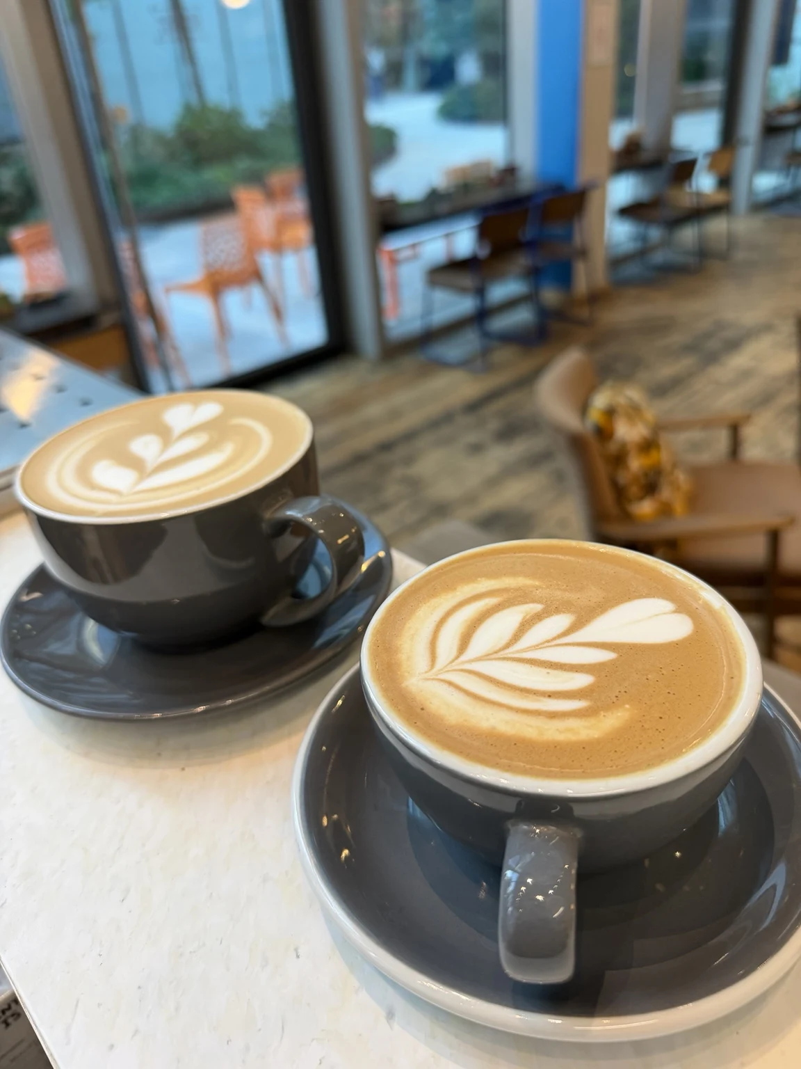 Two grey cups with layered tulip latte art in a bright café